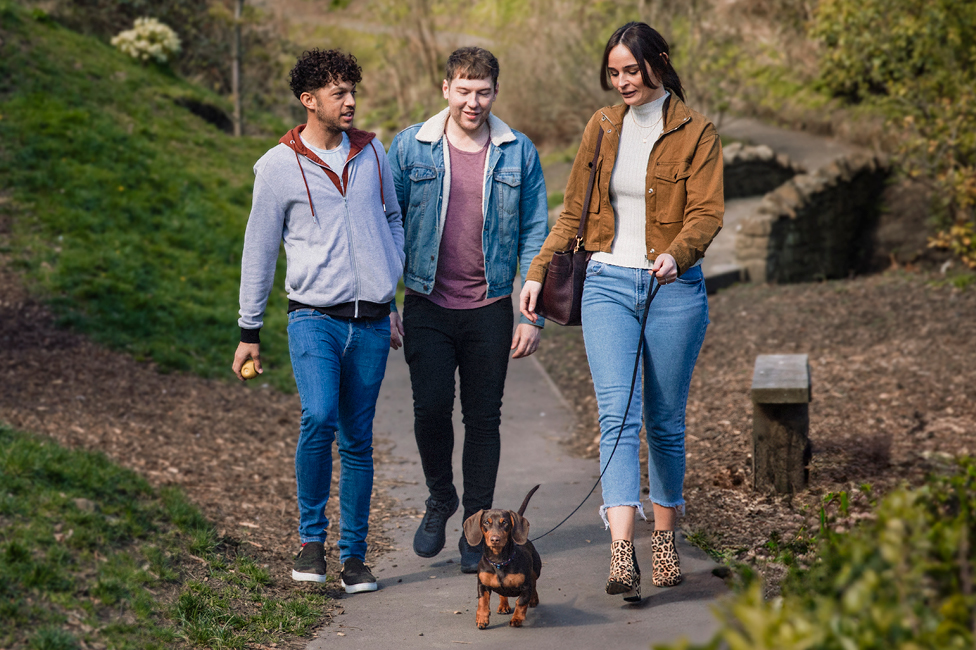 a woman and two men, smiling, while walking a dog on a leash